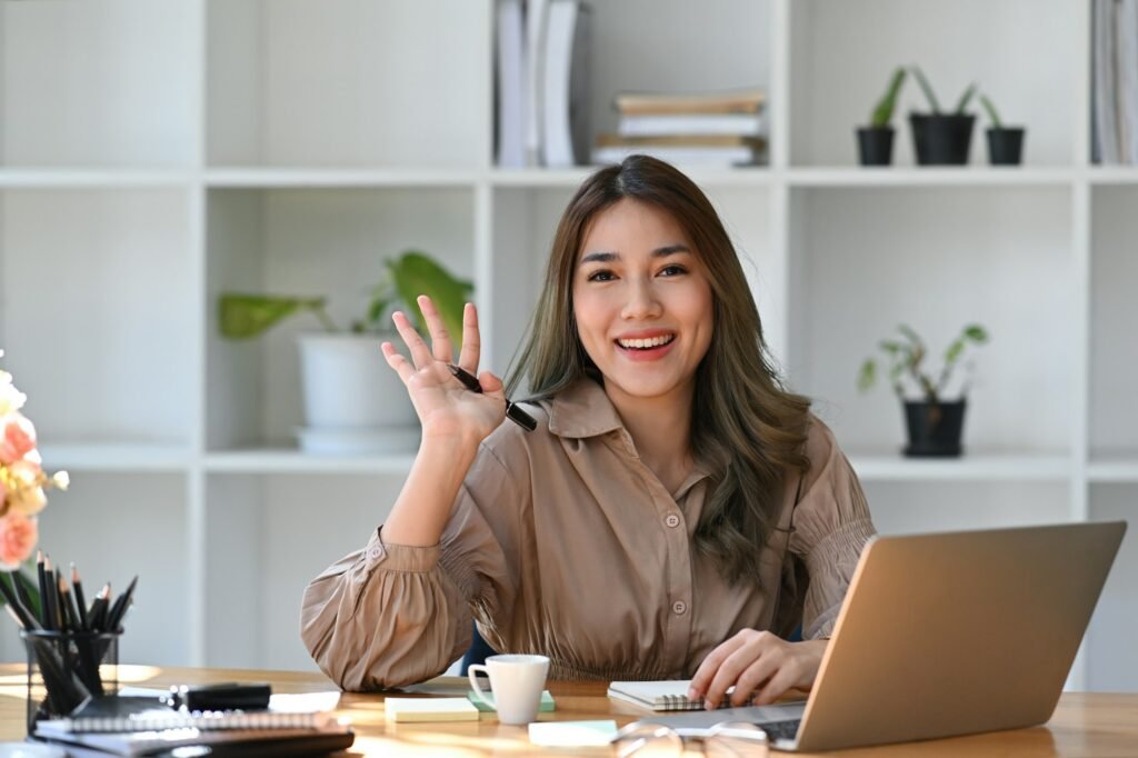 Head shot happy businesswoman waving her hand and smiling to camera.