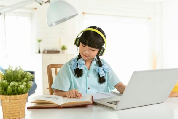 Homeschool Asian little young girl student learning virtual internet online class on table at home.