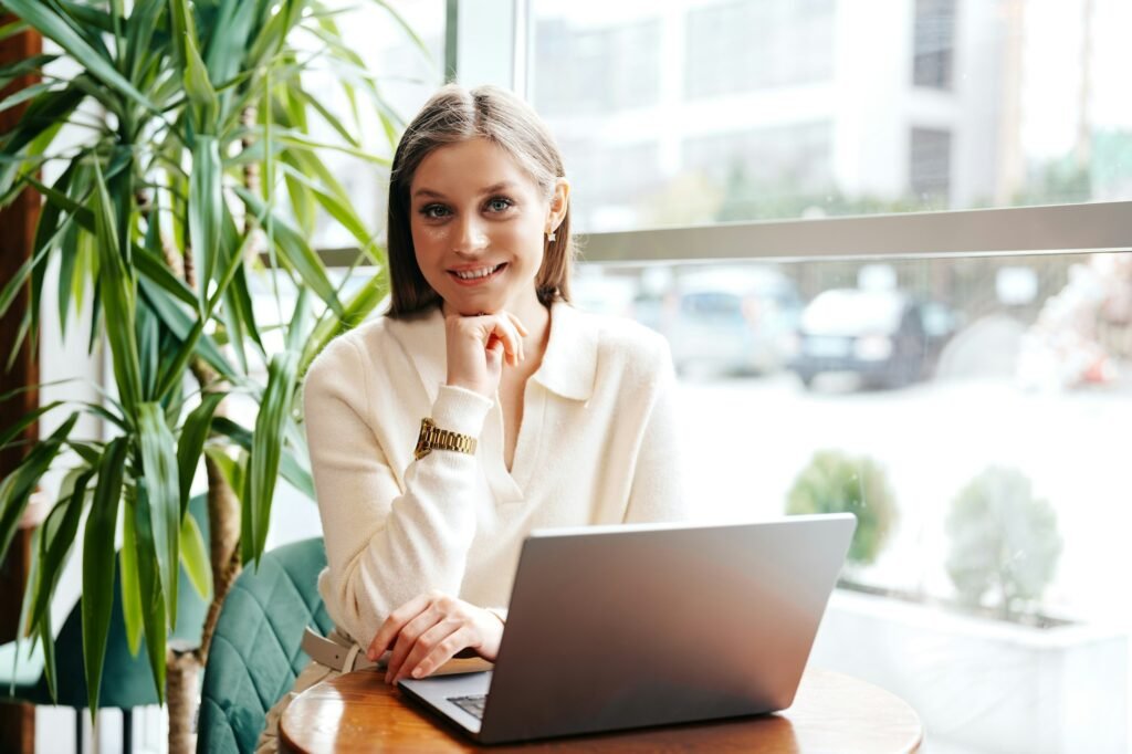 Smiling Young Woman Working on Laptop at Cozy Cafe During Daytime